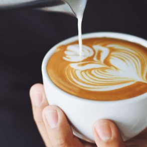 A barista pouring a flower shape into a cup of coffee with cream.