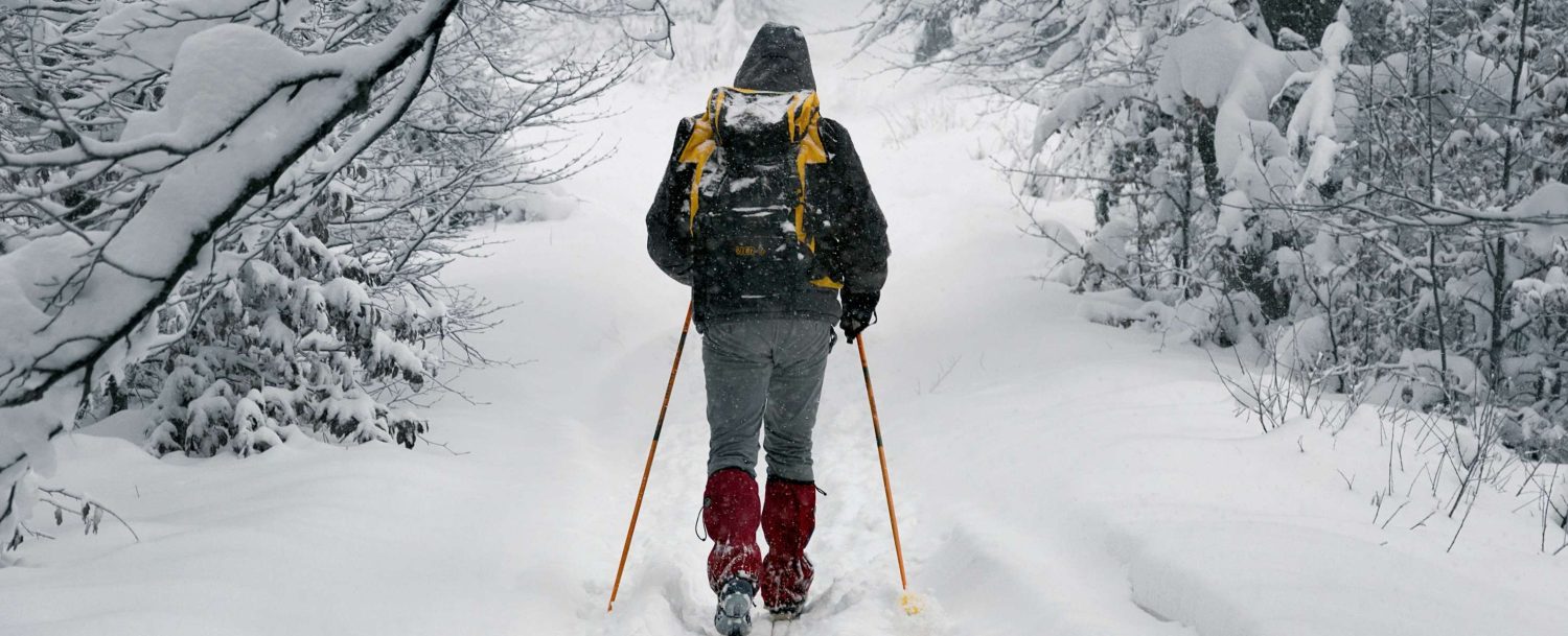 Man trudging through a snow covered trail on skis in West Michigan