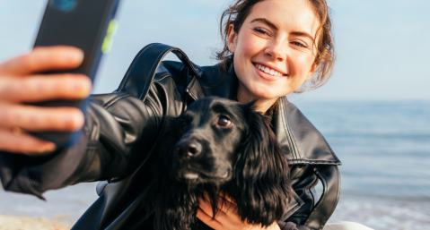 woman taking a selfie with dog on beach
