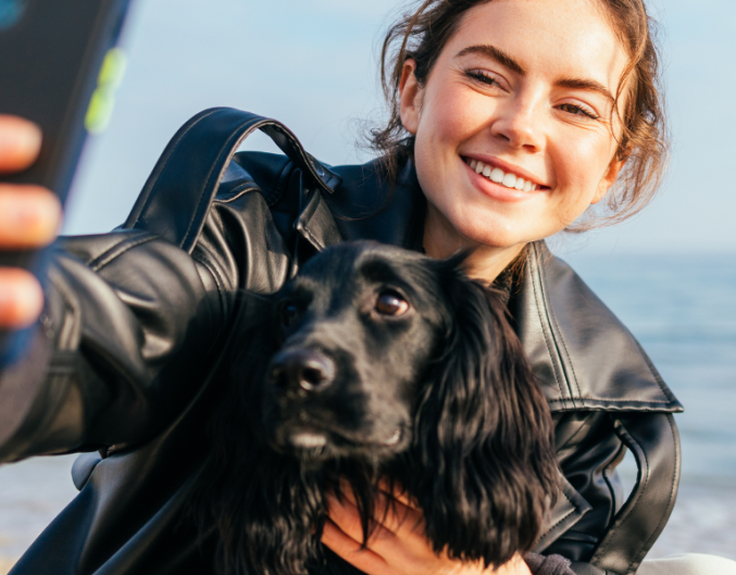 woman taking a selfie with dog on beach
