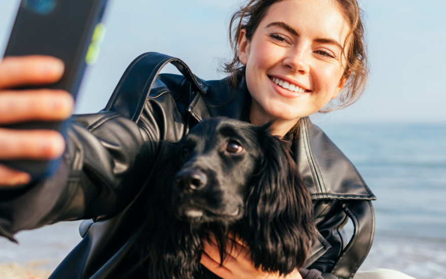 woman taking a selfie with dog on beach