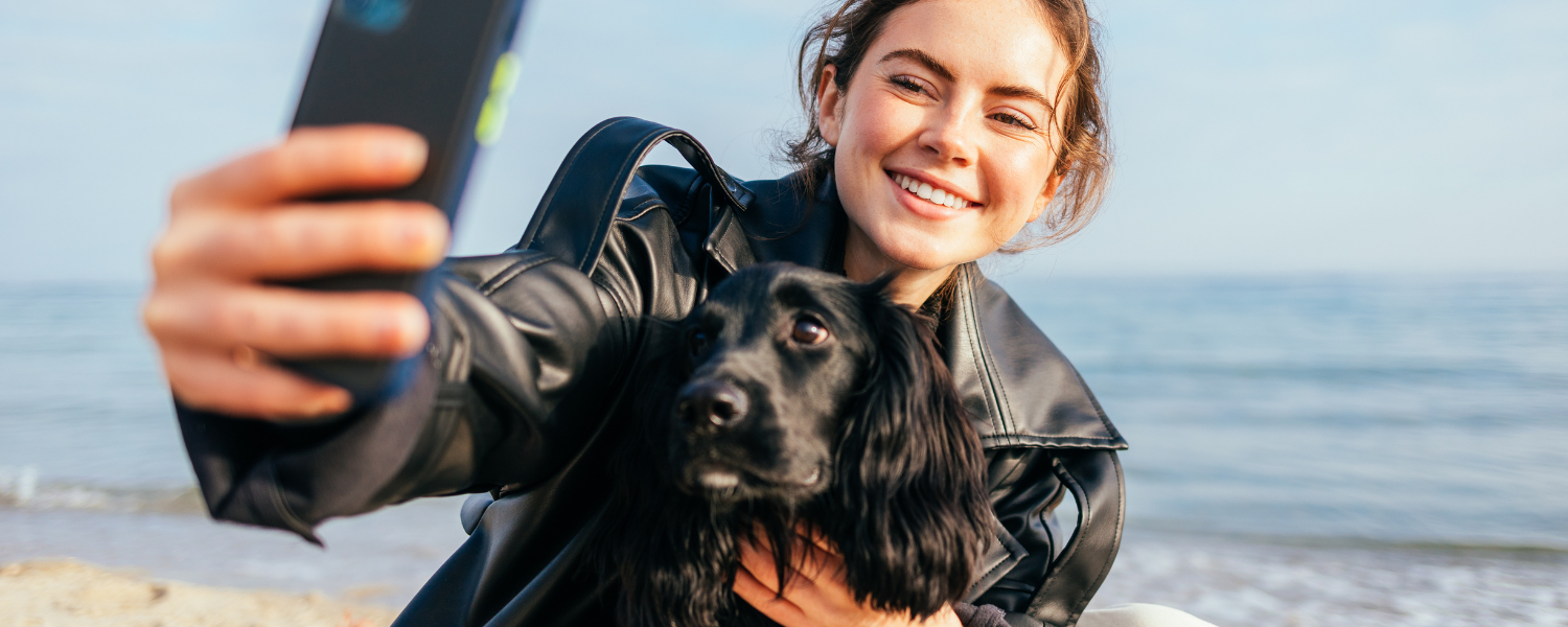 woman taking a selfie with dog on beach