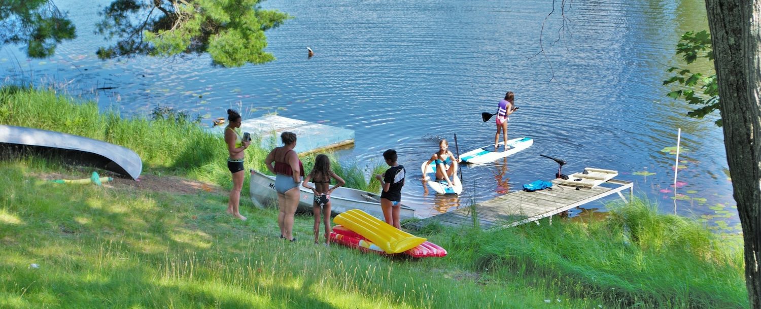 Parents watching children jump off a dock and swim in a lake.