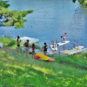 Parents watching children jump off a dock and swim in a lake.