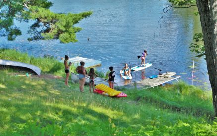 Parents watching children jump off a dock and swim in a lake.