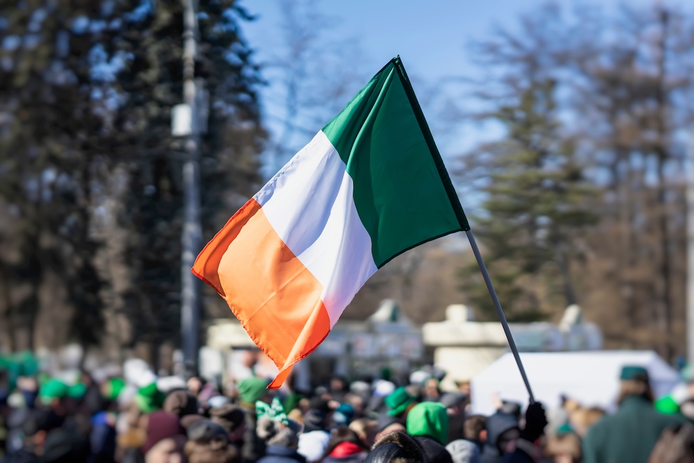 Flag of Ireland close-up in hands on background of blue sky during the celebration.