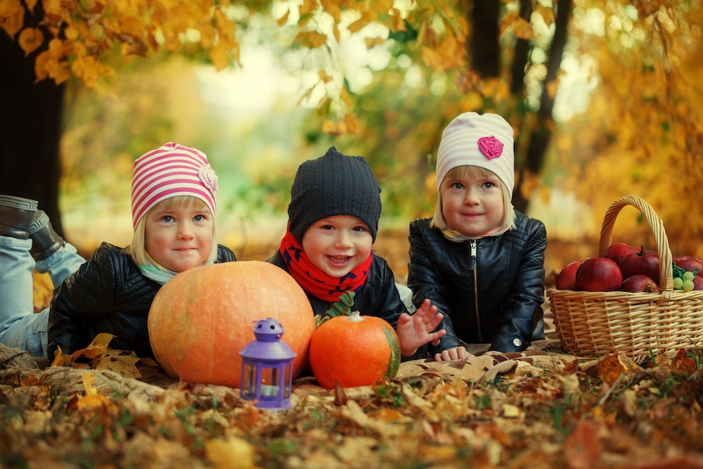 Three friends kids lying on autumn leaves with pumpkins and apple.