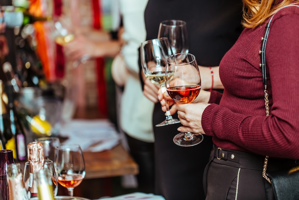 wine tasting: visitors stand near tables with tasting samples and hold glasses of wine.